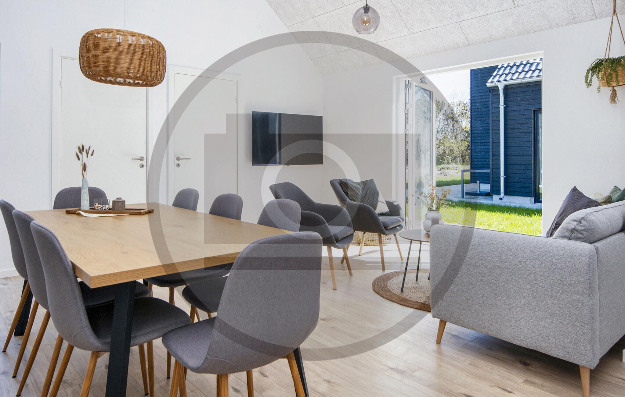 A modern dining area with a wooden table and grey upholstered chairs, a hanging wicker light fixture, and a television mounted on the wall.