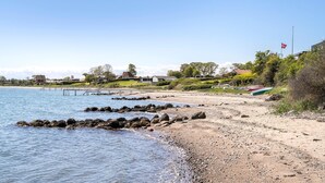 A coastal beach with a rocky shoreline, a pier, and houses in the background. - 2 bedroom cozy home in Juelsminde (Juelsminde)