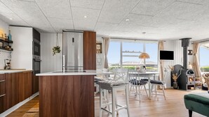 A modern kitchen with a central island, a dining area with white chairs, and a cozy seating area with a green sofa. - 2 bedroom cozy home in Juelsminde (Juelsminde)