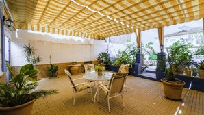 Un patio techado con toldo a cuadros, plantas en macetas y una mesa redonda con sillas.