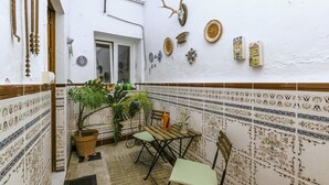 Un pequeño patio amurallado con suelo de baldosas, una mesa de madera con sillas, plantas en macetas y varios adornos en las paredes, incluyendo una cabeza de venado y adornos con forma de casa.