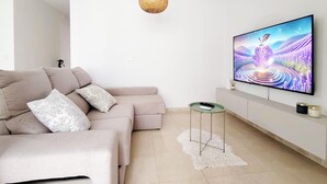 Moderni olohuone, jossa on beigenvärinen kulmasohva, seinälle asennettu taulutelevisio, pieni sivupöytä ja koristeellinen matto.