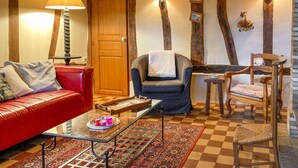 Un salon chaleureux avec un canapé rouge, un fauteuil bleu, une chaise en bois, une table basse en verre et un tapis à motifs.