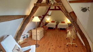 Une chambre confortable située sous les combles, avec des poutres apparentes, deux lits, une chaise, une lampe et une petite table.