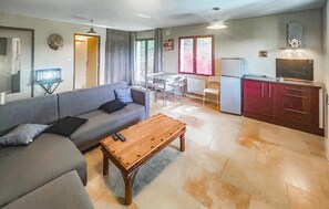 Un salon avec un canapé, une table basse en bois, une cuisine équipée d’un réfrigérateur et un coin repas avec des chaises et une table.