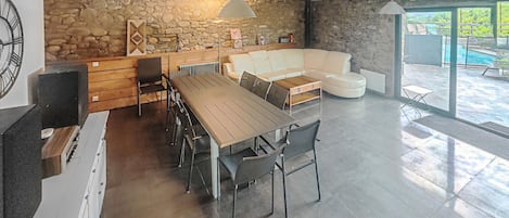 A modern kitchen with a stone wall, a dining area with a long table and chairs, and a large window overlooking a pool.