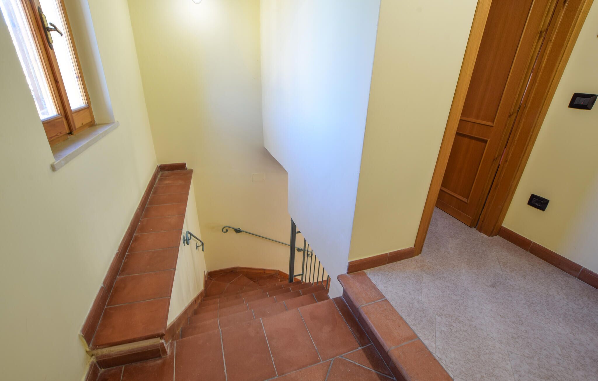 Una escalera con baldosas de terracota y barandilla, que conduce a una puerta con marco de madera.