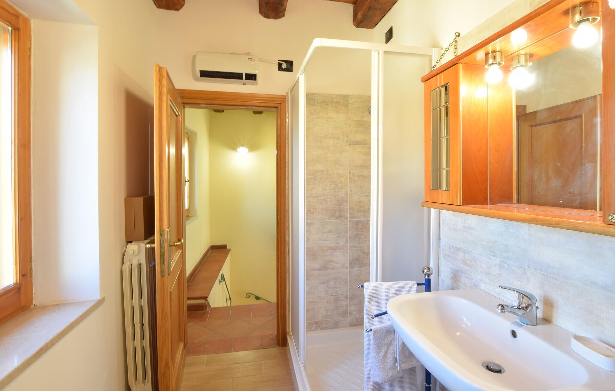 Un baño con un lavabo blanco, armarios de madera y una zona de ducha.