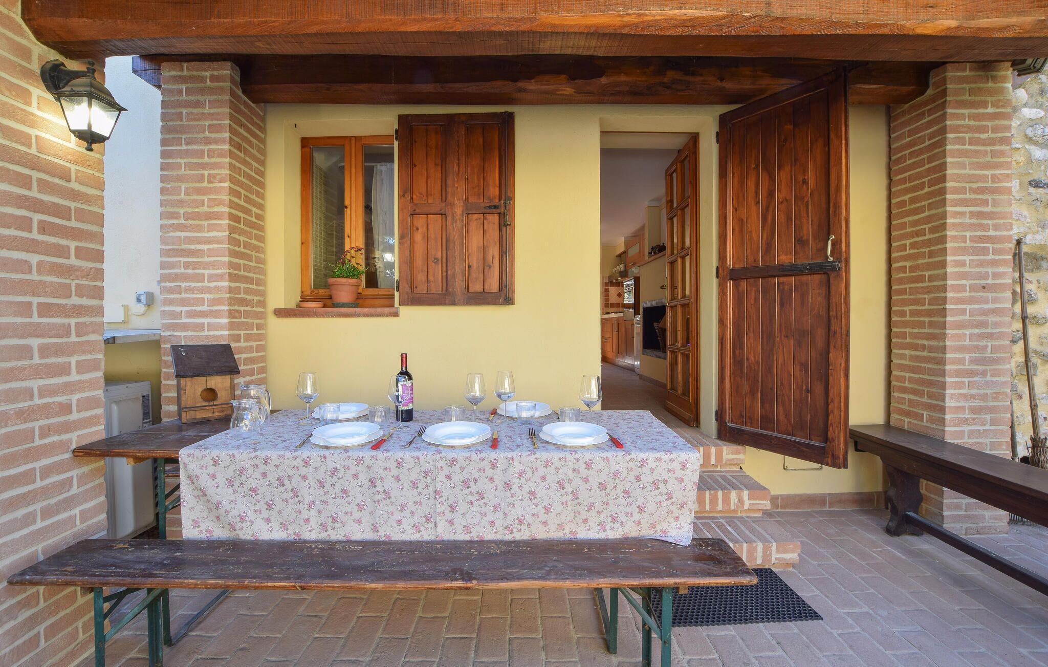 Un espace de restauration en plein air avec une table dressée pour quatre personnes, une bouteille de vin et un banc.