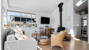 A modern living room with a sofa, a wicker chair, a television, and a fireplace. - 2 bedroom cozy home in Otterup (Otterup)