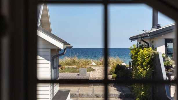 A view through a window with a grid pattern, overlooking a coastal area with a clear sky and calm sea. - 2 bedroom cozy home in Otterup (Otterup)