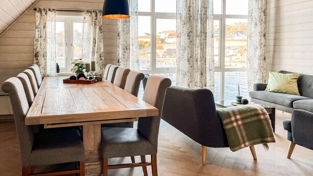 A dining area with a wooden table, multiple chairs, and a view of a body of water through large windows. - 3 bedroom beautiful home in Sirevåg (Sirevåg)