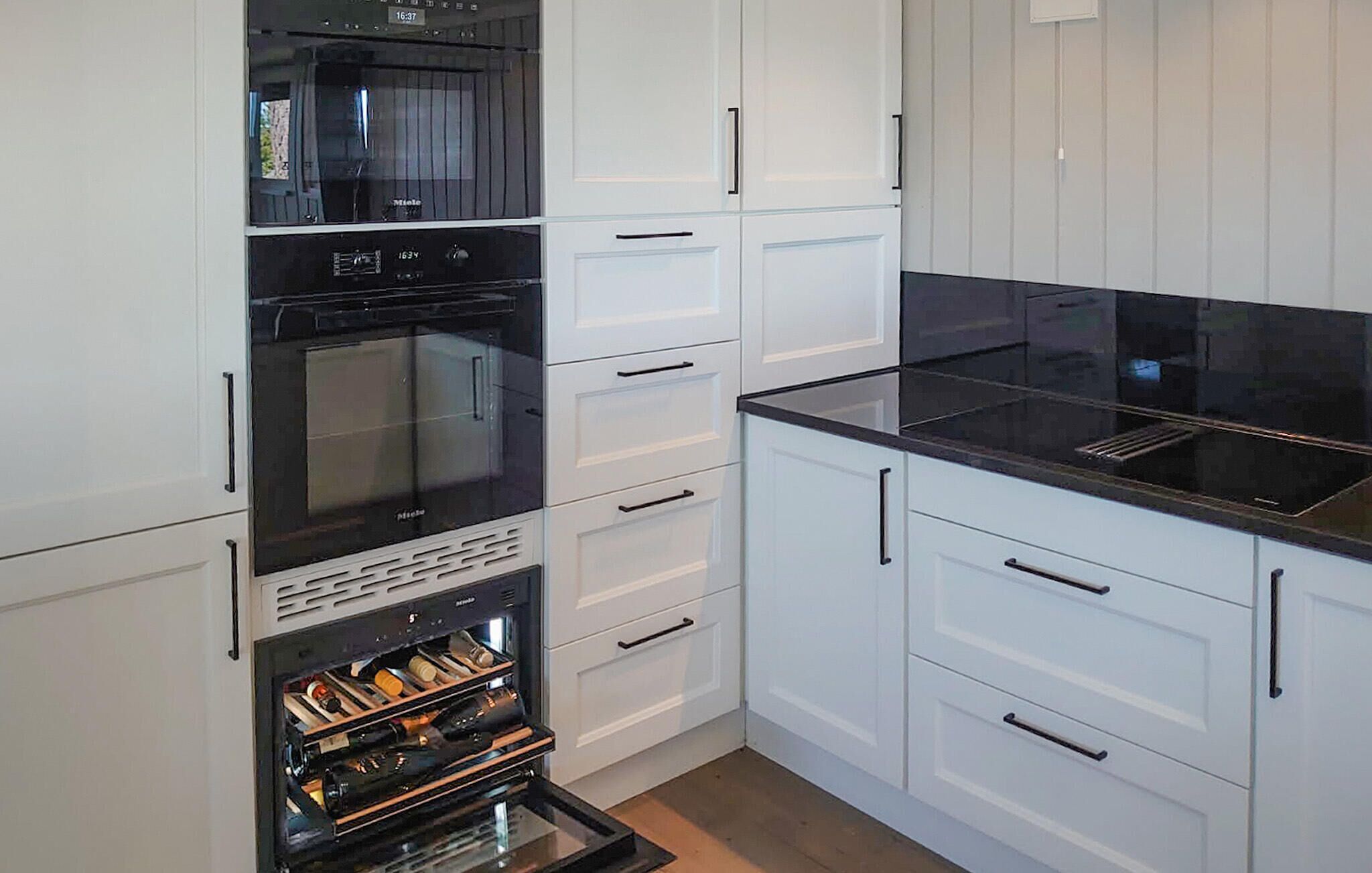 Cozinha moderna com armários brancos, bancada preta e eletrodomésticos embutidos, incluindo micro-ondas, forno e climatizador de vinhos.