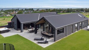 A modern house with a large patio area, a hot tub, and a view of the sea.