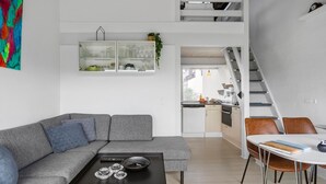 En moderne lejlighed med en grå sofa, et sort sofabord, et spisebord med stole, et køkken og en trappe.