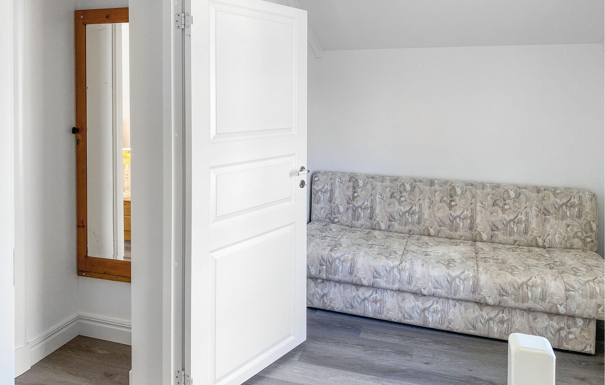 A room with a white door, a patterned sofa, and a wooden floor.