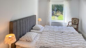 A neatly made bed with a grey headboard, a floral lamp, and a chair with a patterned cushion. - Cozy home in Ormaryd with WiFi (Ormaryd)