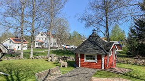 A small red cabin with a thatched roof, a picnic table, and a stone wall in a grassy area with trees and a house in the background. - Cozy home in Ormaryd with WiFi (Ormaryd)