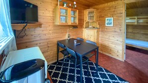 Ein Holzblockhaus-Interieur mit Esstisch, Stühlen, Fernseher, Schränken und einem gemusterten Teppich.