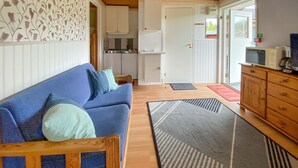 A cozy living area with a blue sofa, a wooden cabinet, and a kitchen in the background.