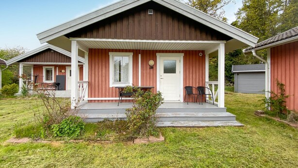 A two-story wooden house with a porch, a front door, and a small garden area.
