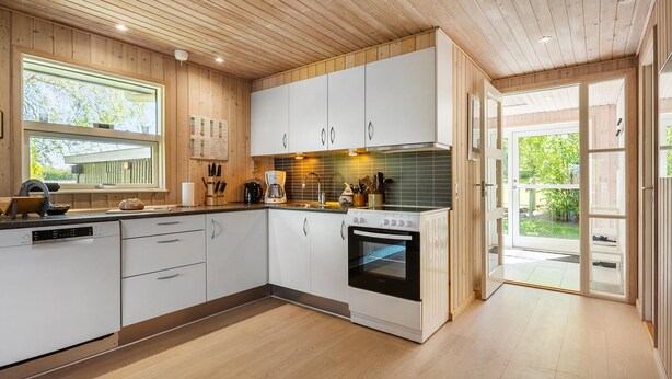 Une cuisine moderne avec des meubles en bois, un four encastré et une grande fenêtre donnant sur un jardin.