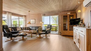 Un salon moderne avec un plafond en bois, des canapés en cuir, une table à manger et un téléviseur posé sur un meuble.