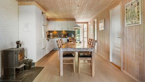 Une cuisine moderne avec des meubles blancs, une table à manger en bois et un poêle à bois.
