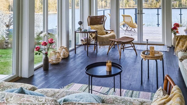 A cozy, well-lit room with large windows overlooking a lake, furnished with wicker chairs, a sofa, and a small round table. - Cozy home in Värmdö with sauna (Värmdö)