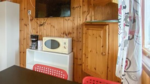 Une petite pièce avec un mur en bois, un four à micro-ondes, une machine à café et une chaise rouge.