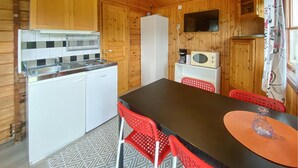 Une cuisine compacte équipée d’un réfrigérateur, d’un four à micro-ondes et d’une machine à café. On y trouve une table à manger avec des chaises rouges et un tapis à motifs.