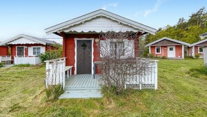 Une petite maison de plain-pied, à l’extérieur rouge et aux ornements blancs, dotée d’un porche avec un banc et d’un petit arbre devant.