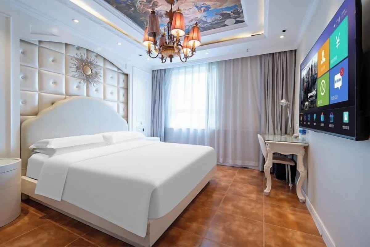 Ein modernes Hotelzimmer mit einem großen Bett, einem Schreibtisch und einem digitalen Bildschirm, der Informationen zum Zimmer anzeigt.