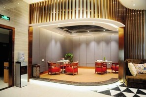 Eine Hotelhalle mit einer Rezeption, einer Sitzecke mit roten Stühlen und einem Sofa.