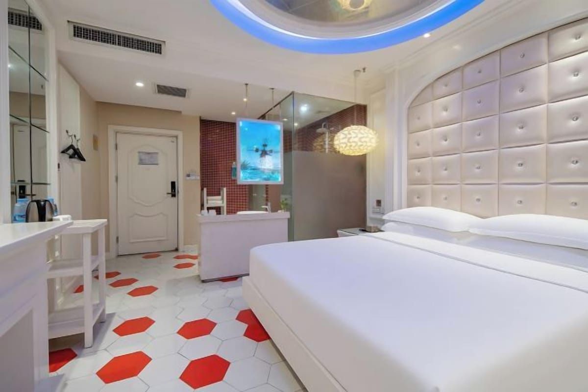 Ein modernes Hotelzimmer mit einem großen Bett, einem Schminktisch mit Spiegel, einem kleinen Schreibtisch und einem einzigartigen, sechseckig gemusterten Boden.