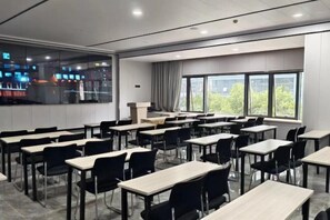 Een klaslokaal met rijen bureaus en stoelen, grote ramen en uitzicht op de stadsgezicht.