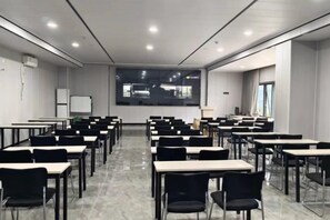 Un salón de conferencias con mesas y sillas dispuestas para reuniones, una pizarra y una pantalla de proyección.
