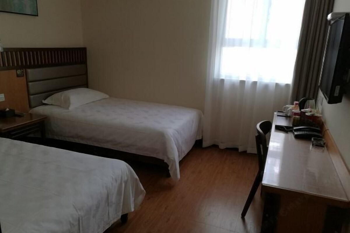 Habitación de hotel con dos camas individuales, un escritorio de madera, una silla y un televisor montado en la pared.