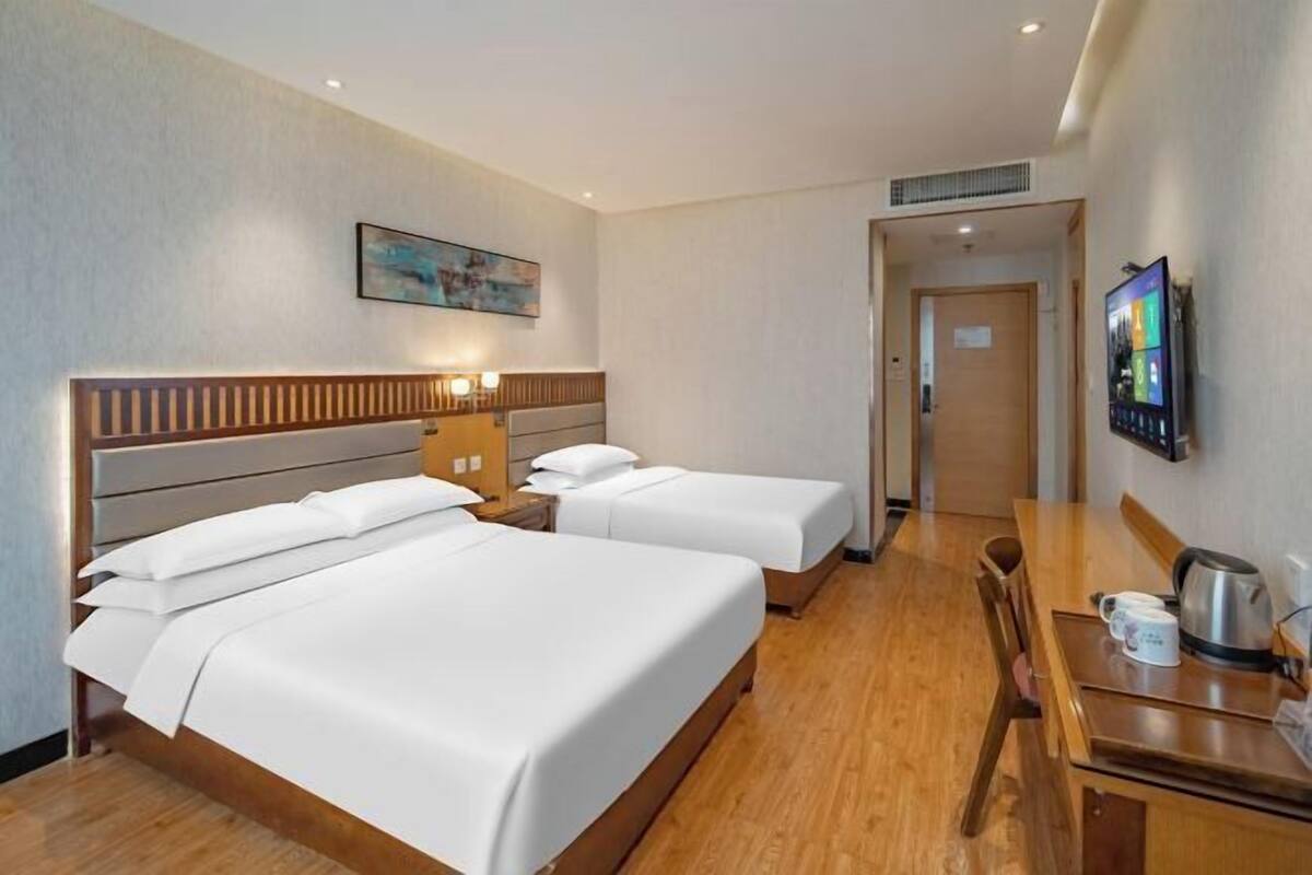 Een hotelkamer met twee bedden, een houten hoofdbord, een bureau met een stoel, een televisie en een schilderij aan de muur.