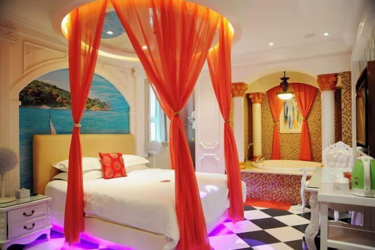 Een slaapkamer met een hemelbed, een grote spiegel, een wastafel en een kaptafel.