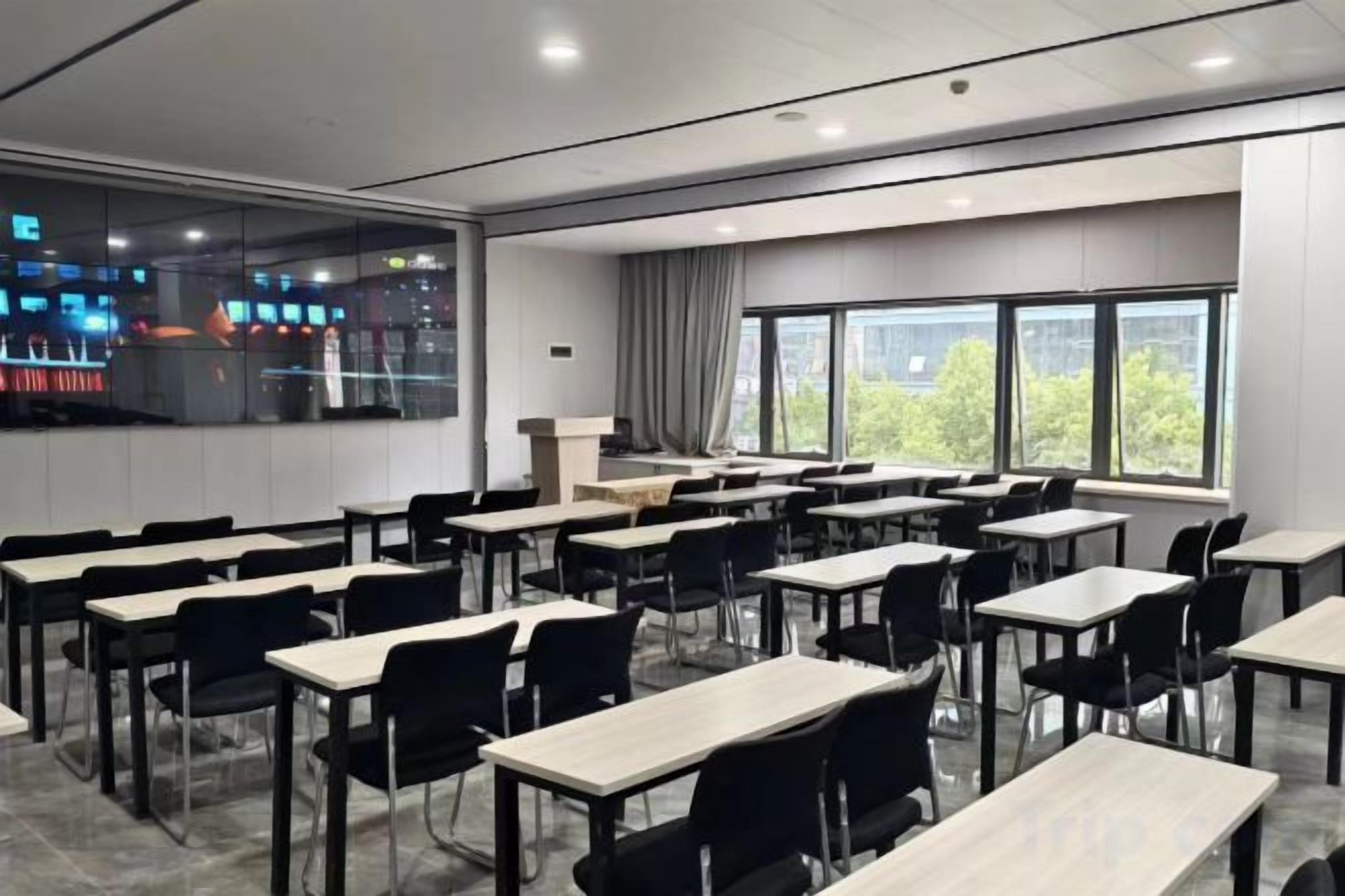 A classroom with multiple tables and chairs, large windows, and a view of the outside.