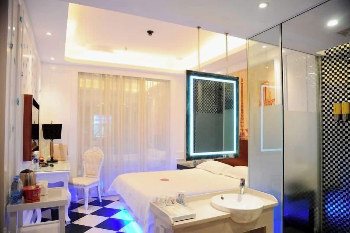 Een hotelkamer met een bed, nachtkastje, stoel en een grote spiegel.