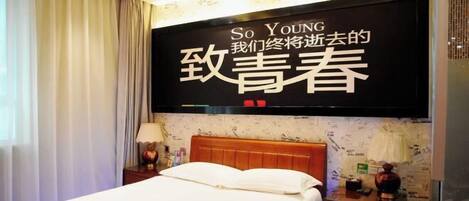 A hotel room with a bed, a nightstand, a lamp, and a wall-mounted TV displaying text.