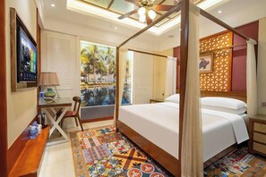 A bedroom with a canopy bed, a desk with a chair, a television, and a view of a palm tree.