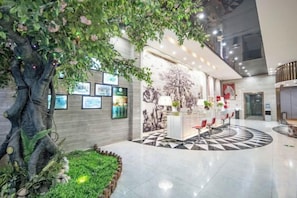 A lobby with a central reception desk, a large tree, and a patterned floor. - Yi Cheng Hotel (Xinbai Square Subway Station Store, Shijiazhuang) (Shijiazhuang)