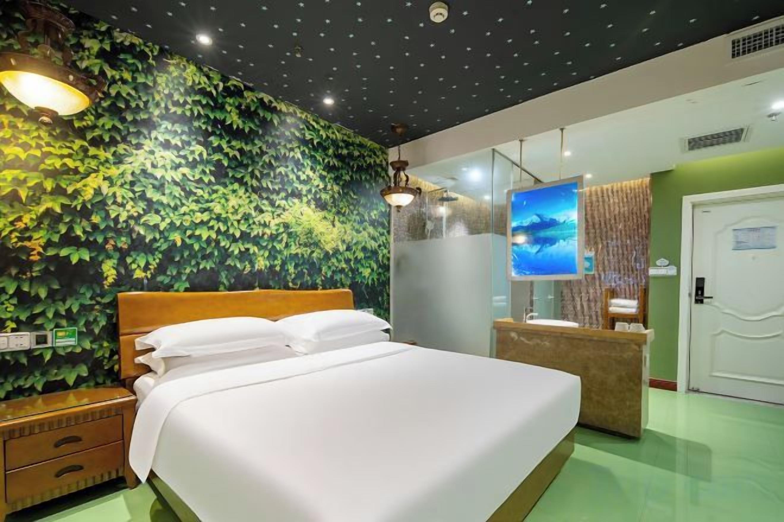 Una camera d'albergo con un letto, una reception, una televisione e una parete verdeggiante.