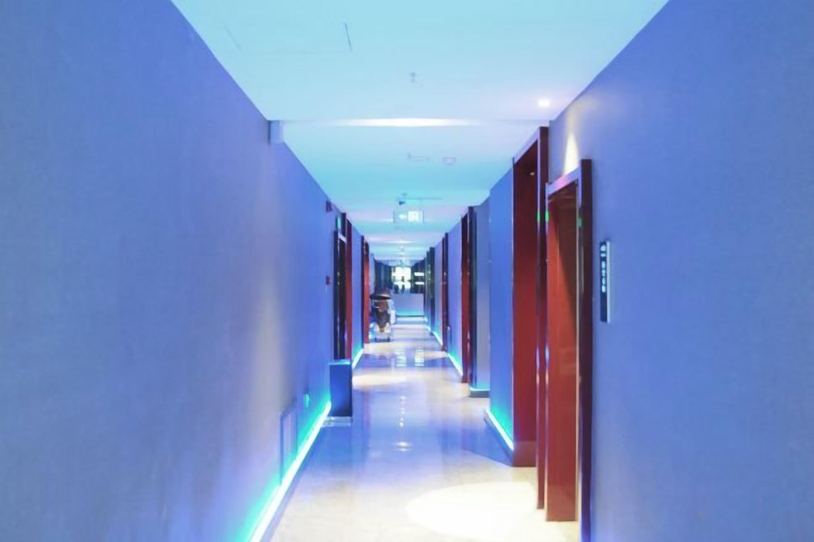 A hotel corridor with a modern design, featuring a long hallway with doors on both sides and a central walkway.