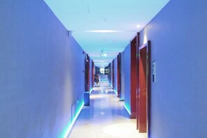 A hotel corridor with a modern design, featuring a long hallway with doors on both sides and a central walkway.