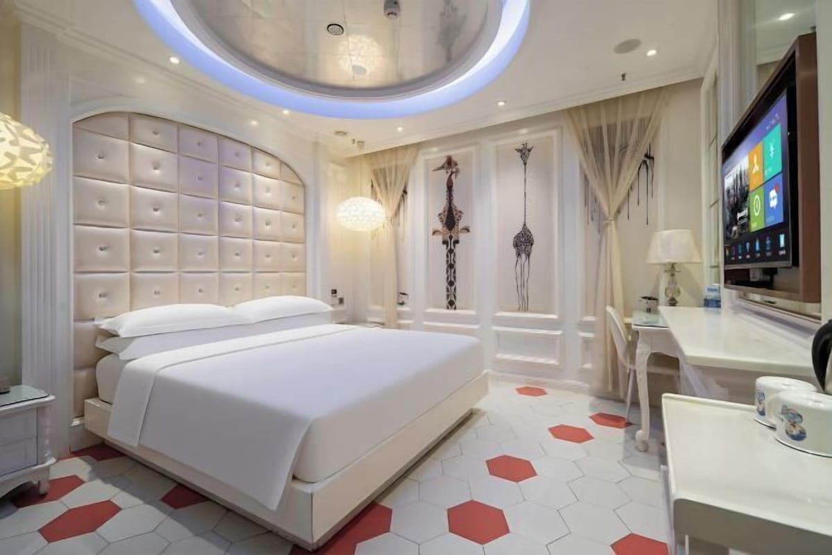 A modern hotel room with a large bed, a desk, and a television.