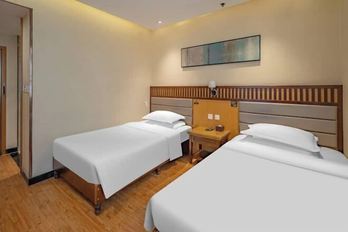 Een hotelkamer met twee eenpersoonsbedden, een houten hoofdeinde, een nachtkastje met een lamp en een schilderij aan de muur.